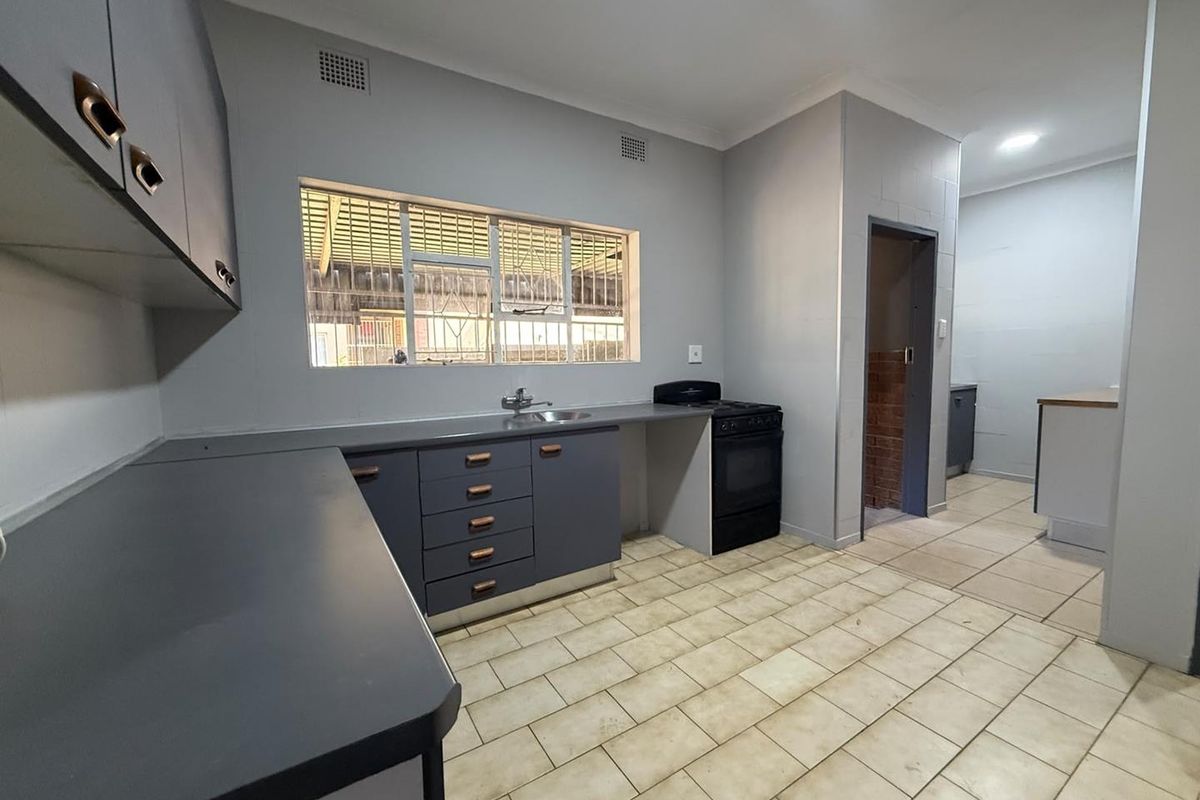 A functional kitchen featuring grey cabinetry, laminate countertops, a freestanding stove, and tiled flooring, offering a clean and practical workspace.