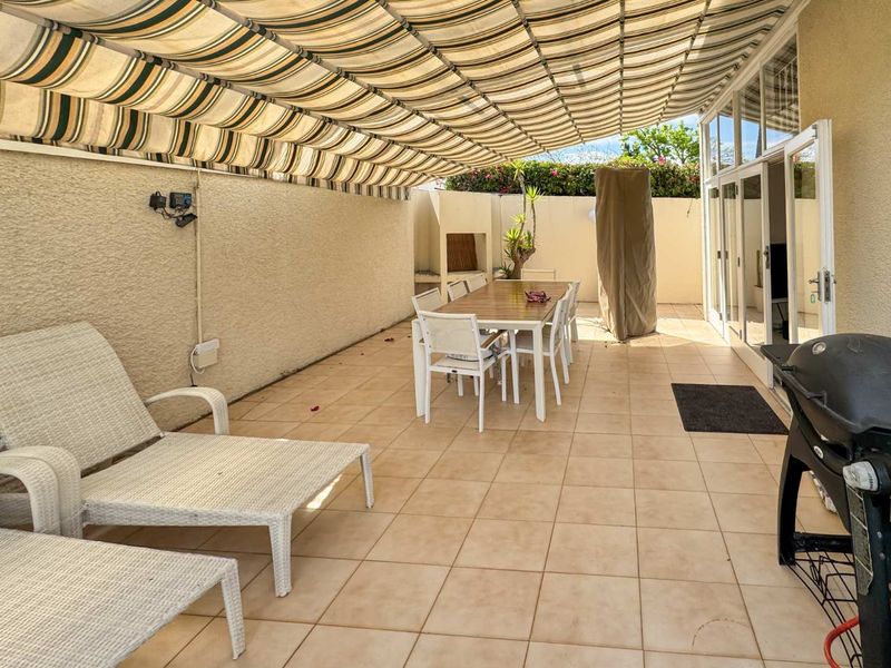 Covered outdoor patio featuring tiled flooring, a built-in braai, and a retractable awning, providing a functional space for outdoor dining and relaxation.