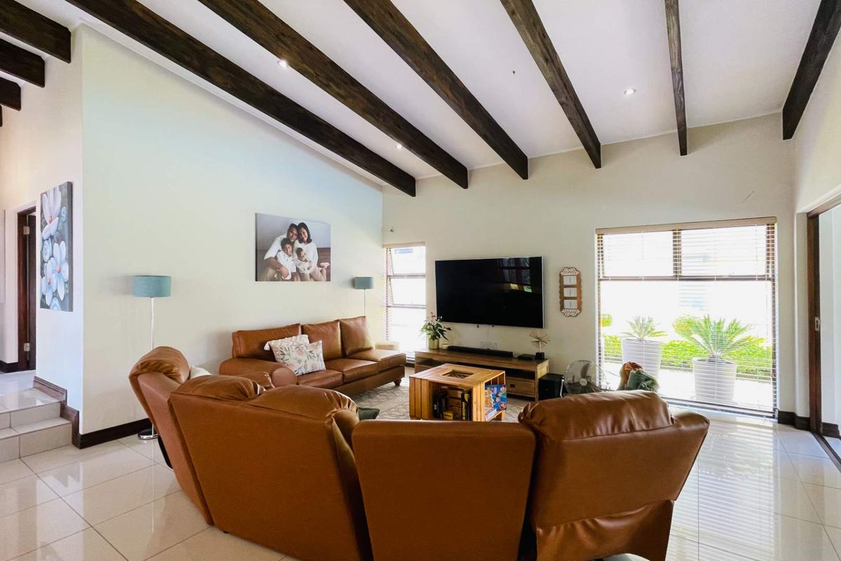 Spacious living room featuring high vaulted ceilings with exposed timber beams, large format floor tiles, and sliding glass doors leading to the outdoor area.