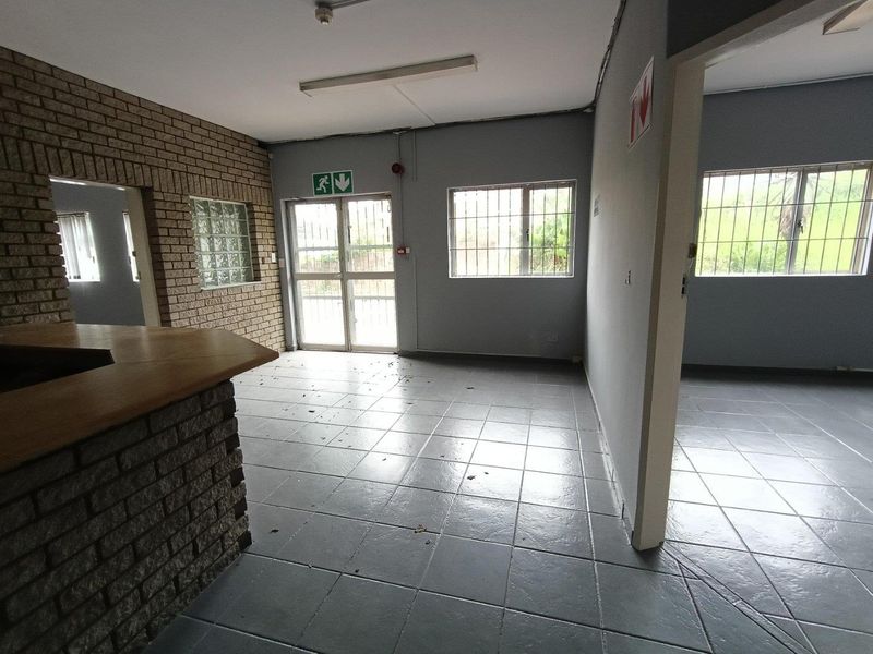 An empty industrial office space featuring tiled flooring, a brick feature wall, built-in counter, and security bars on windows and doors.