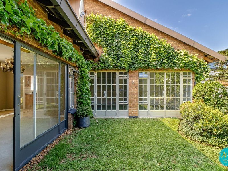 A private rear garden area featuring a brick facade, lush climbing ivy, and multiple glass door access points to the interior living spaces.