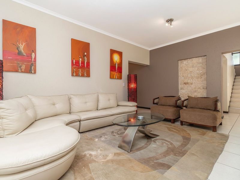 Spacious living room featuring a stone accent wall, neutral tiled flooring, and a staircase leading to the upper level.