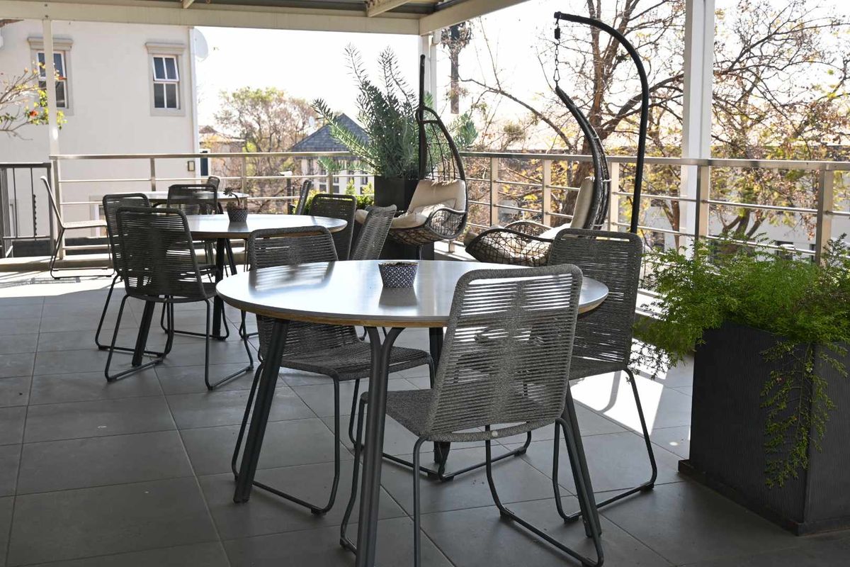 A spacious covered balcony featuring tiled flooring and a modern stainless steel railing, providing an ideal outdoor area for office staff breaks.