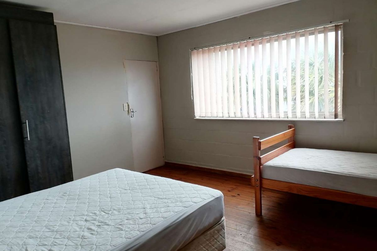 A functional bedroom featuring timber flooring, built-in cabinetry, and vertical window blinds, offering a neutral space ready for personalization.