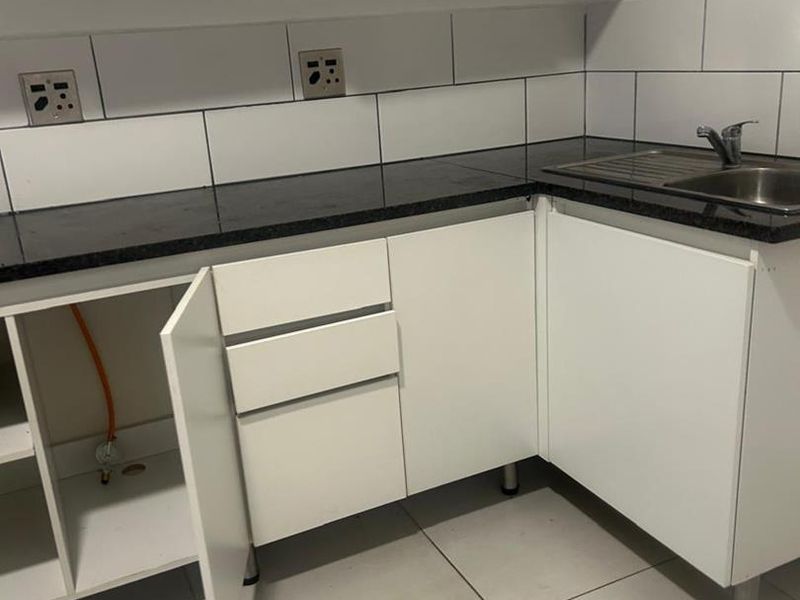 A compact kitchen featuring white cabinetry, granite countertops, a stainless steel sink, and subway tile backsplash, currently requiring minor repairs and finishing.