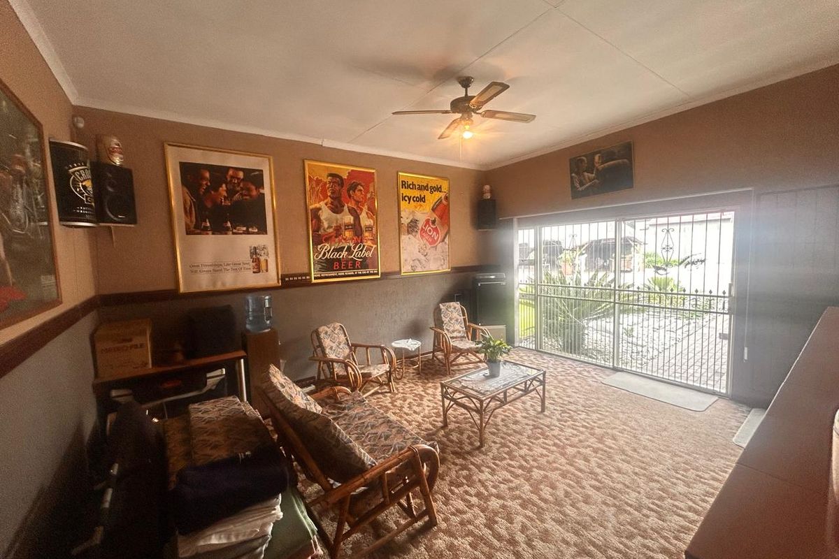 A living room featuring a ceiling fan, large sliding glass doors with security gate, and wall-to-wall carpeting.