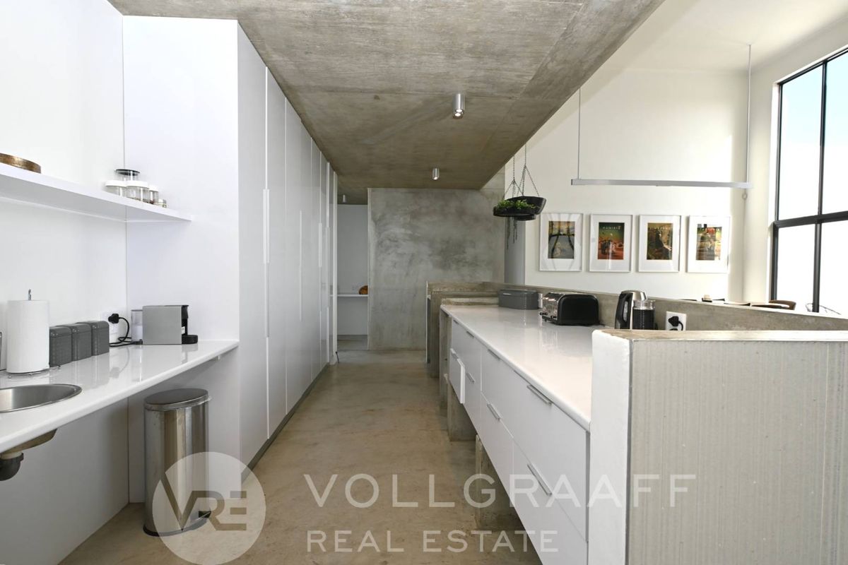 Modern kitchen featuring sleek white cabinetry, polished concrete flooring, exposed concrete ceiling, and integrated stone countertops in a contemporary industrial-style space.
