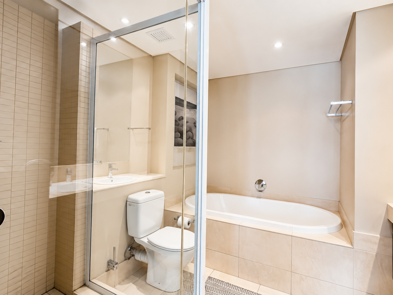 Modern bathroom featuring a built-in bathtub, glass-enclosed shower, vanity with basin, and neutral tiled finishes.