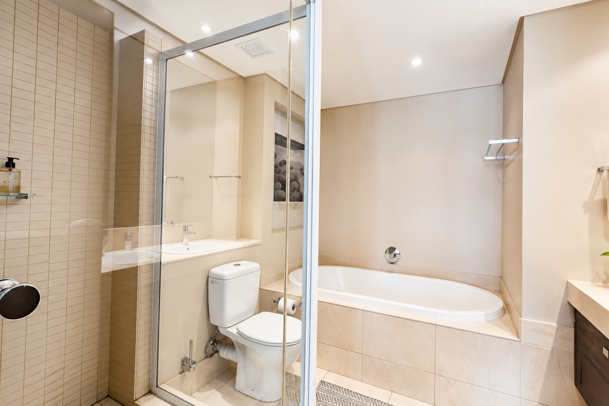 Modern bathroom featuring a built-in bathtub, glass-enclosed shower, vanity with basin, and neutral tiled finishes.