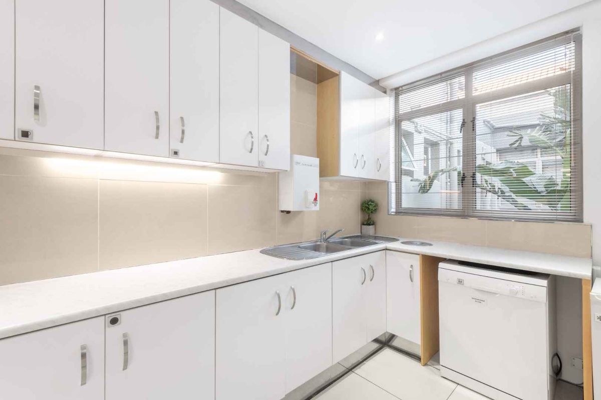 A functional office kitchenette featuring white cabinetry, a stainless steel sink, tiled backsplash, and a large window providing natural light.