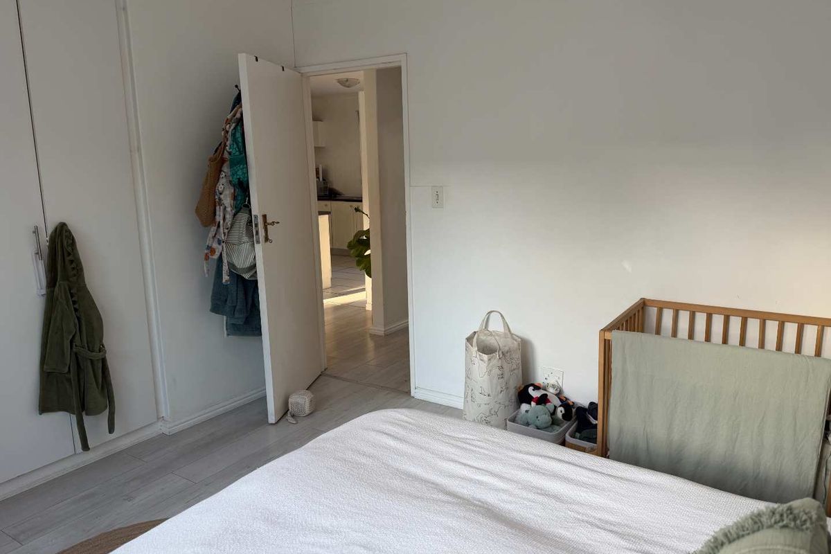 A bedroom featuring built-in cupboards and light-toned laminate flooring, with a doorway leading through to an adjacent kitchen area.