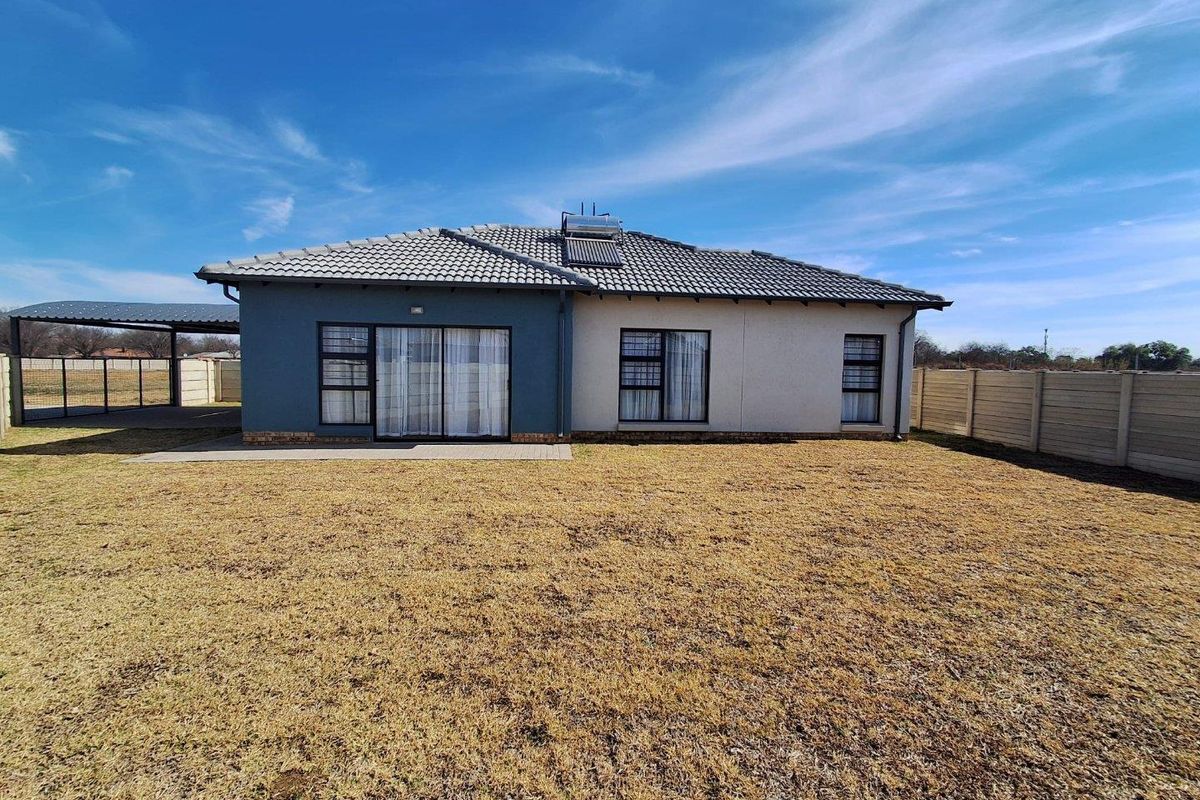 Rear view of a modern single-story house featuring a tiled roof with solar water heating, sliding glass doors, and a spacious backyard.
