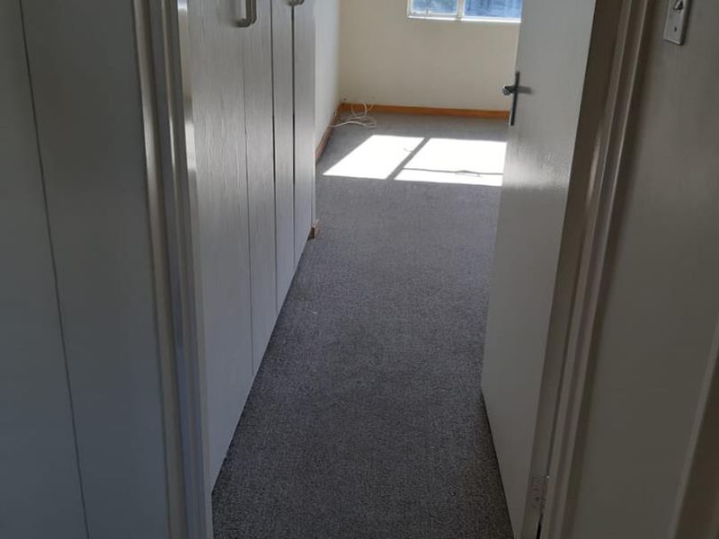 An empty bedroom featuring built-in cupboards, carpeted flooring, and a window allowing natural light.