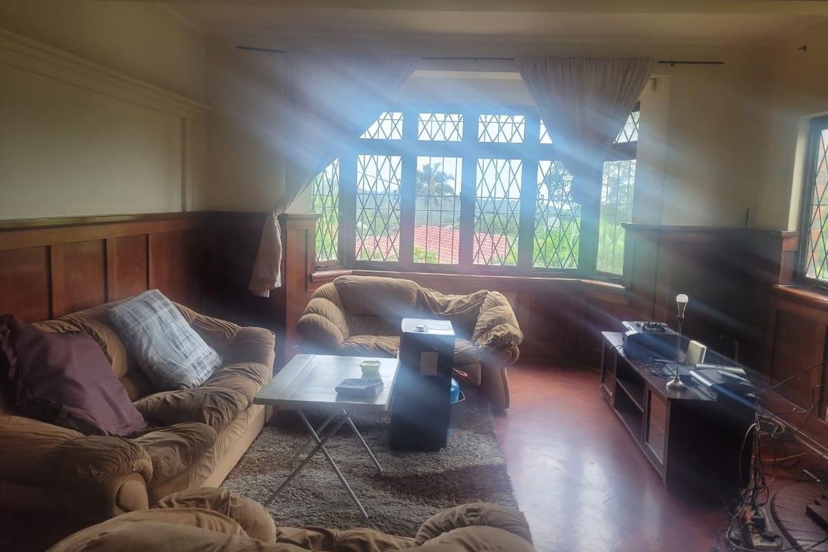 A living room featuring classic timber wall paneling, parquet flooring, and a large leaded glass bay window that provides natural light.