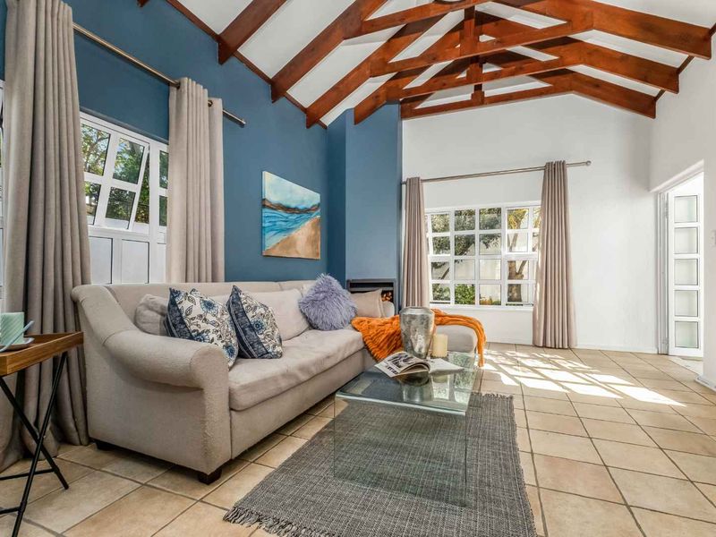Spacious living room featuring high vaulted ceilings with exposed timber rafters, tiled flooring, a cozy fireplace, and large windows providing ample natural light.