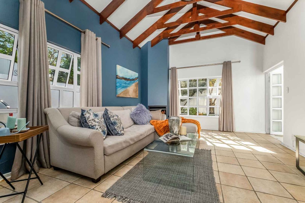 Spacious living room featuring high vaulted ceilings with exposed timber rafters, tiled flooring, a cozy fireplace, and large windows providing ample natural light.