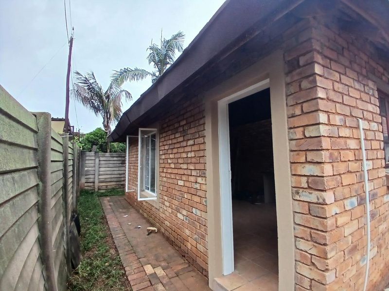 Rear exterior view of the cottage featuring exposed brick walls, a paved walkway, and a precast concrete boundary wall.