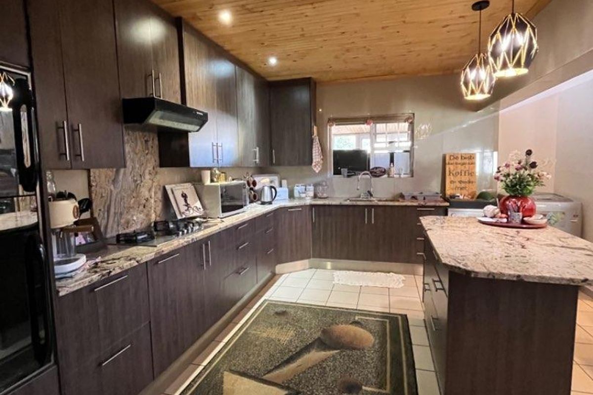 A well-appointed kitchen featuring dark cabinetry, granite countertops, a central island, and a distinctive timber-clad ceiling with recessed and pendant lighting.