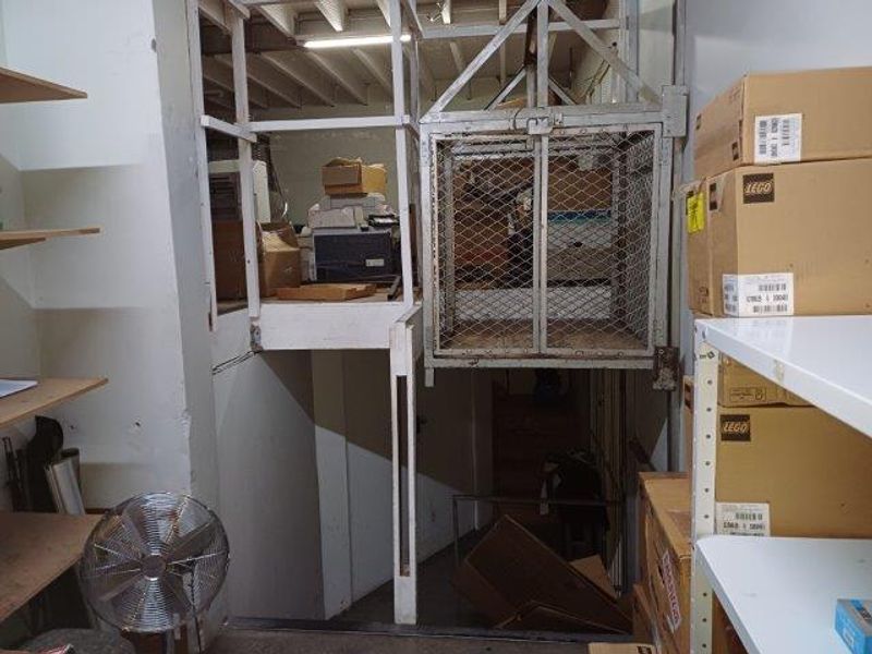Utility area featuring a vintage freight elevator, exposed ceiling joists, and built-in storage shelving in an industrial office setting.