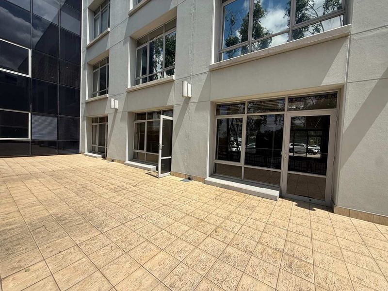 A clean, paved exterior patio area featuring modern aluminium-framed glass doors and windows, providing direct access to the office building interior.