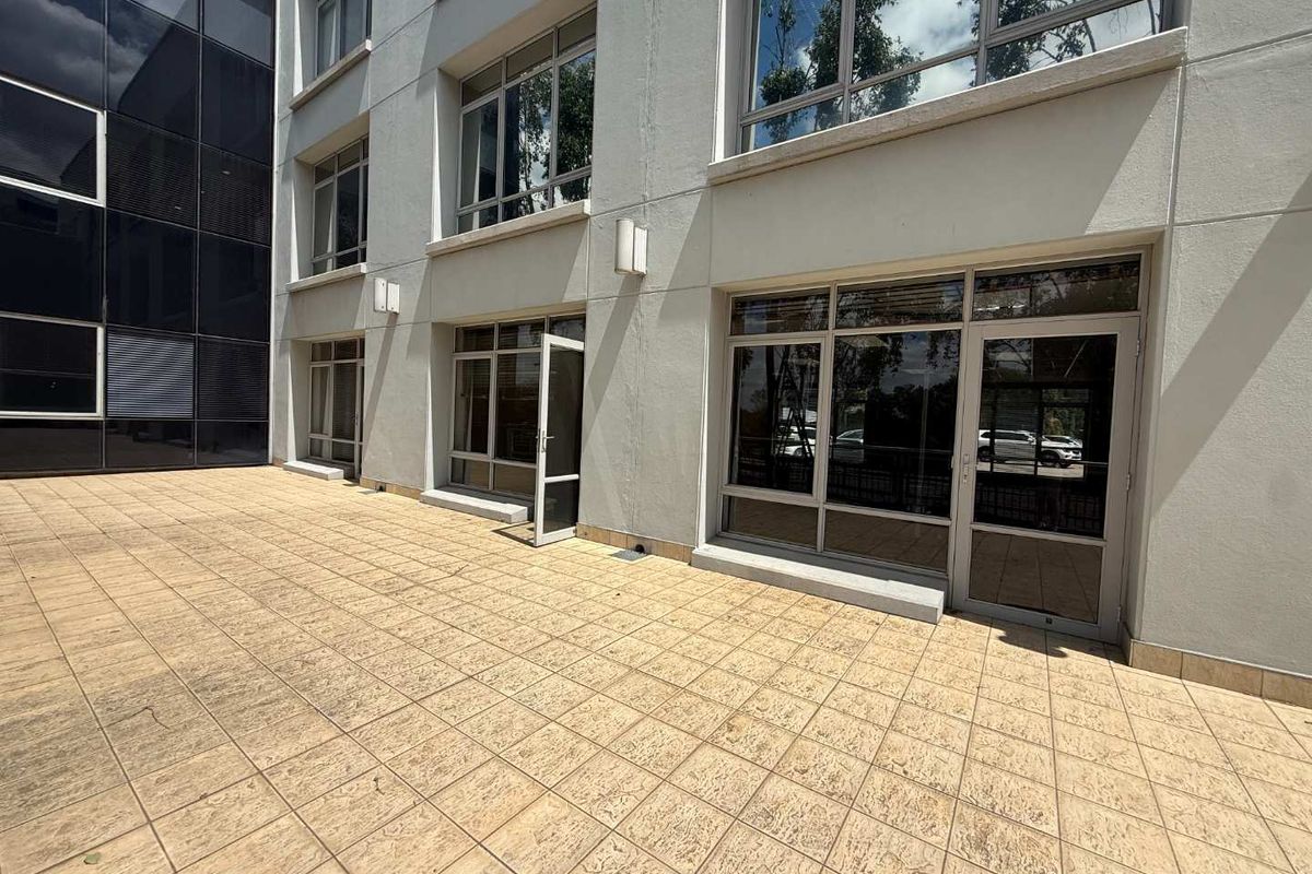 A clean, paved exterior patio area featuring modern aluminium-framed glass doors and windows, providing direct access to the office building interior.