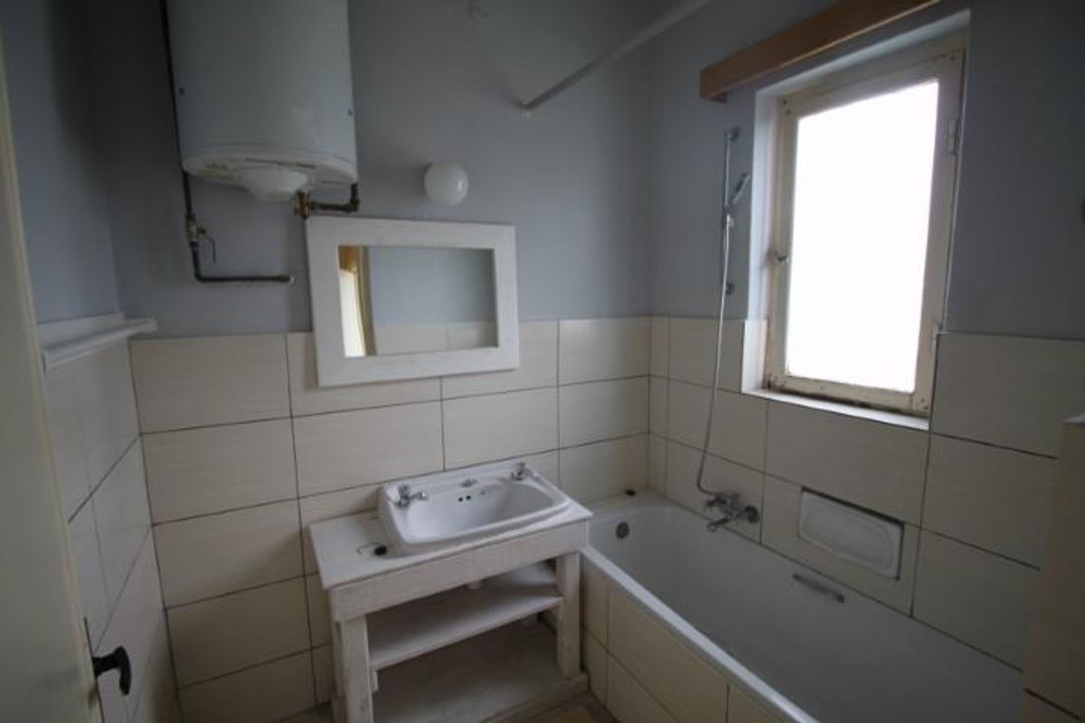 A functional bathroom featuring a bathtub with shower attachment, a wall-mounted basin, and an exposed electric water heater.