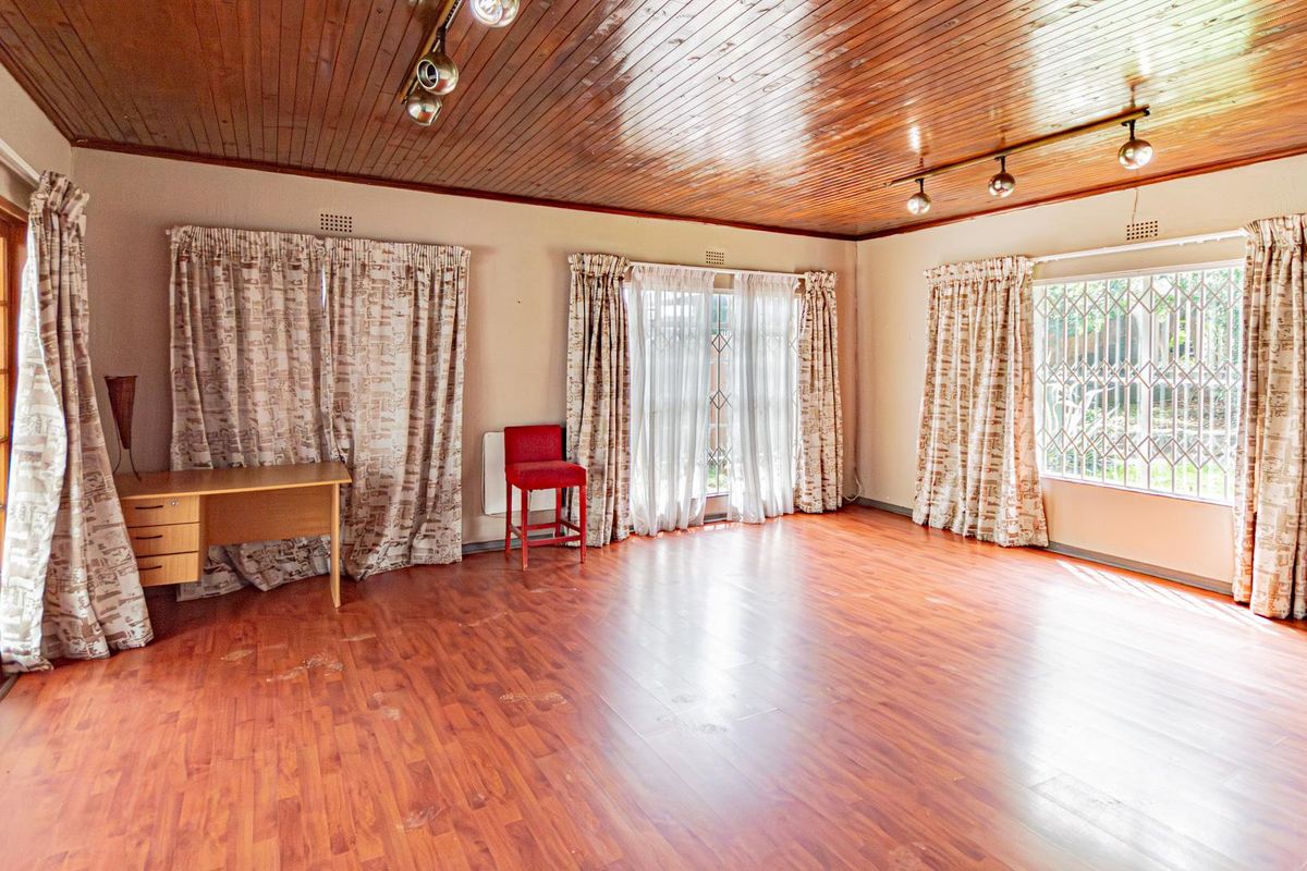 Spacious living room featuring wood-paneled ceilings, laminate flooring, and large windows with security bars, offering a bright and versatile living space.