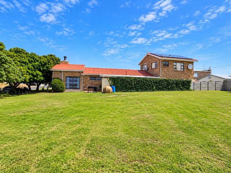 A spacious rear garden view featuring a multi-level brick residential building with a tiled roof, solar panels, and established perimeter boundary walls.