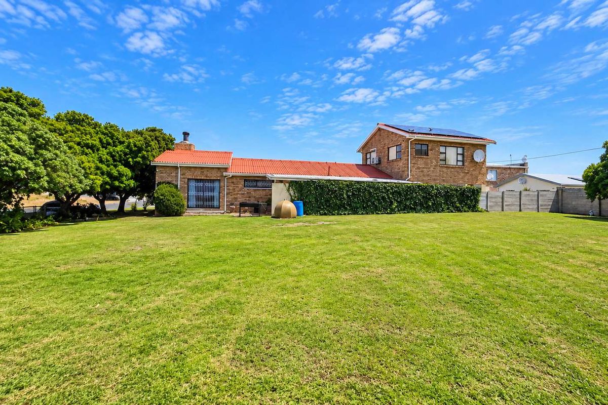 A spacious rear garden view featuring a multi-level brick residential building with a tiled roof, solar panels, and established perimeter boundary walls.