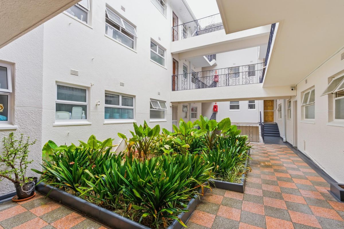 A well-maintained apartment complex courtyard featuring a central garden bed, tiled walkways, and multi-level access balconies with wrought iron railings.