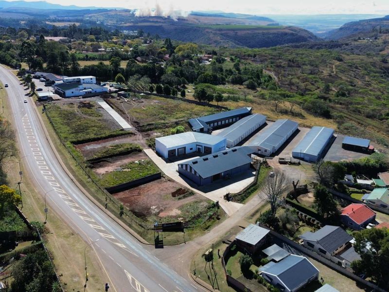 Aerial view of a commercial property featuring multiple warehouse units, paved access, and surrounding landscape with main road frontage.