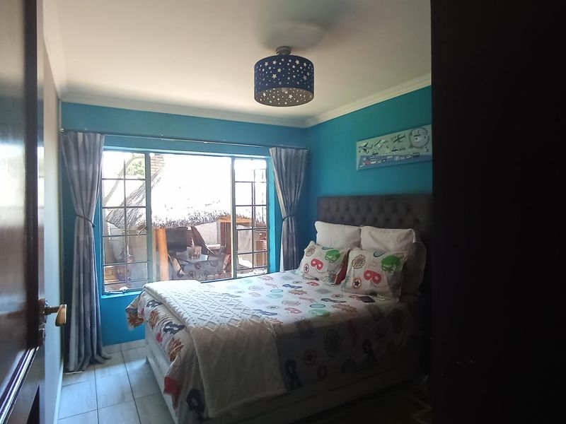 A bedroom featuring tiled flooring, a large metal-framed window, and a central ceiling light fixture, finished with blue accent walls.