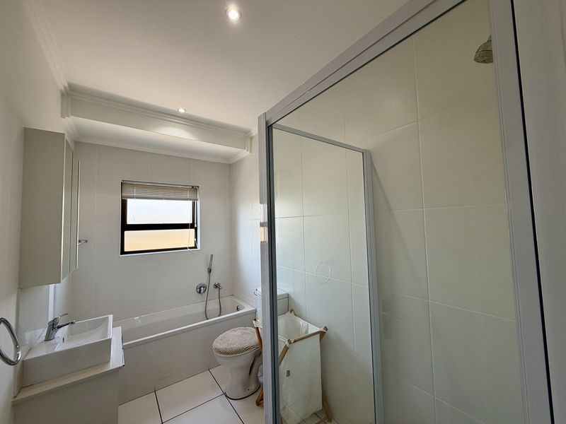 A clean, modern bathroom featuring a built-in bathtub, a separate glass-enclosed shower, and a wall-mounted vanity basin with neutral tiled finishes.