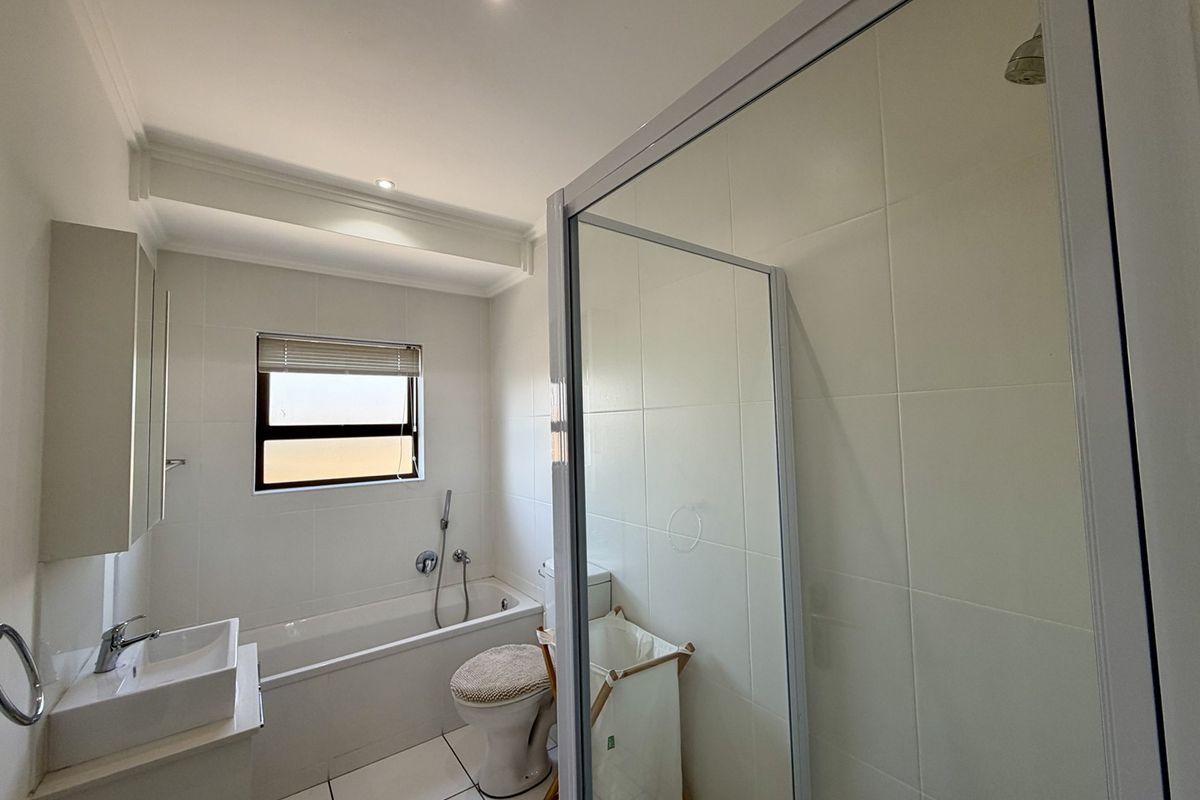 A clean, modern bathroom featuring a built-in bathtub, a separate glass-enclosed shower, and a wall-mounted vanity basin with neutral tiled finishes.