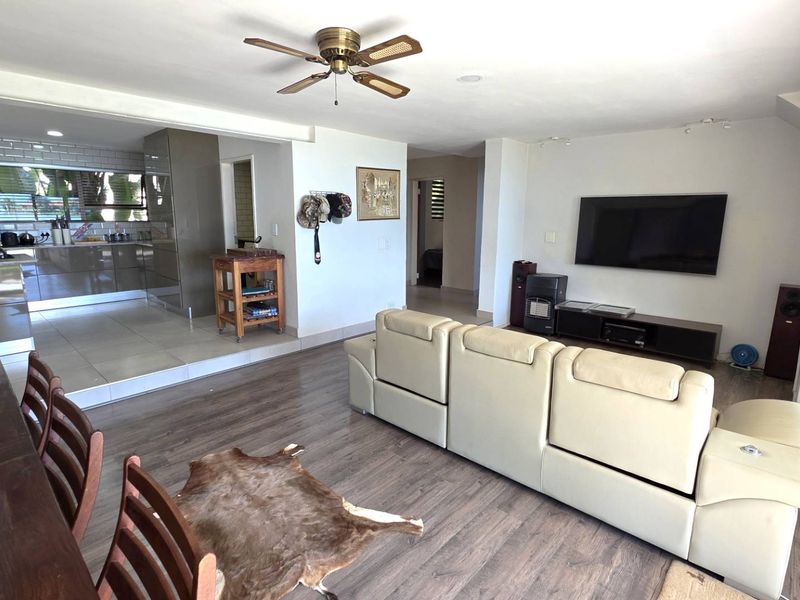 Spacious open-plan living and dining area featuring laminate flooring, a modern kitchen with subway tile backsplash, and large sliding doors leading outdoors.