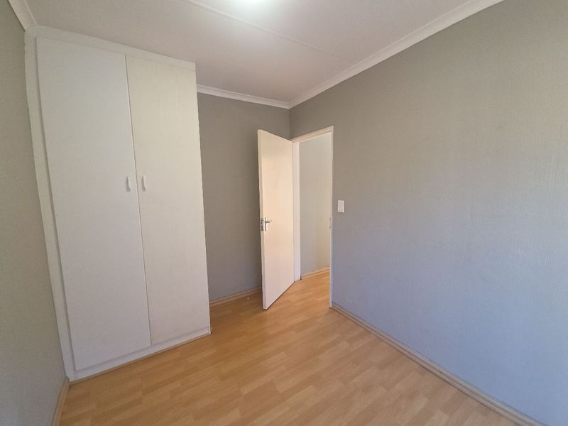 A clean, empty bedroom featuring neutral grey walls, light laminate flooring, and built-in storage cupboards.