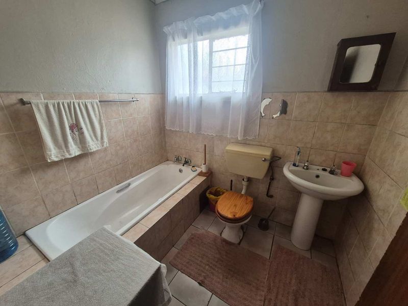 A functional bathroom featuring a built-in bathtub, pedestal sink, and toilet with neutral wall and floor tiling.