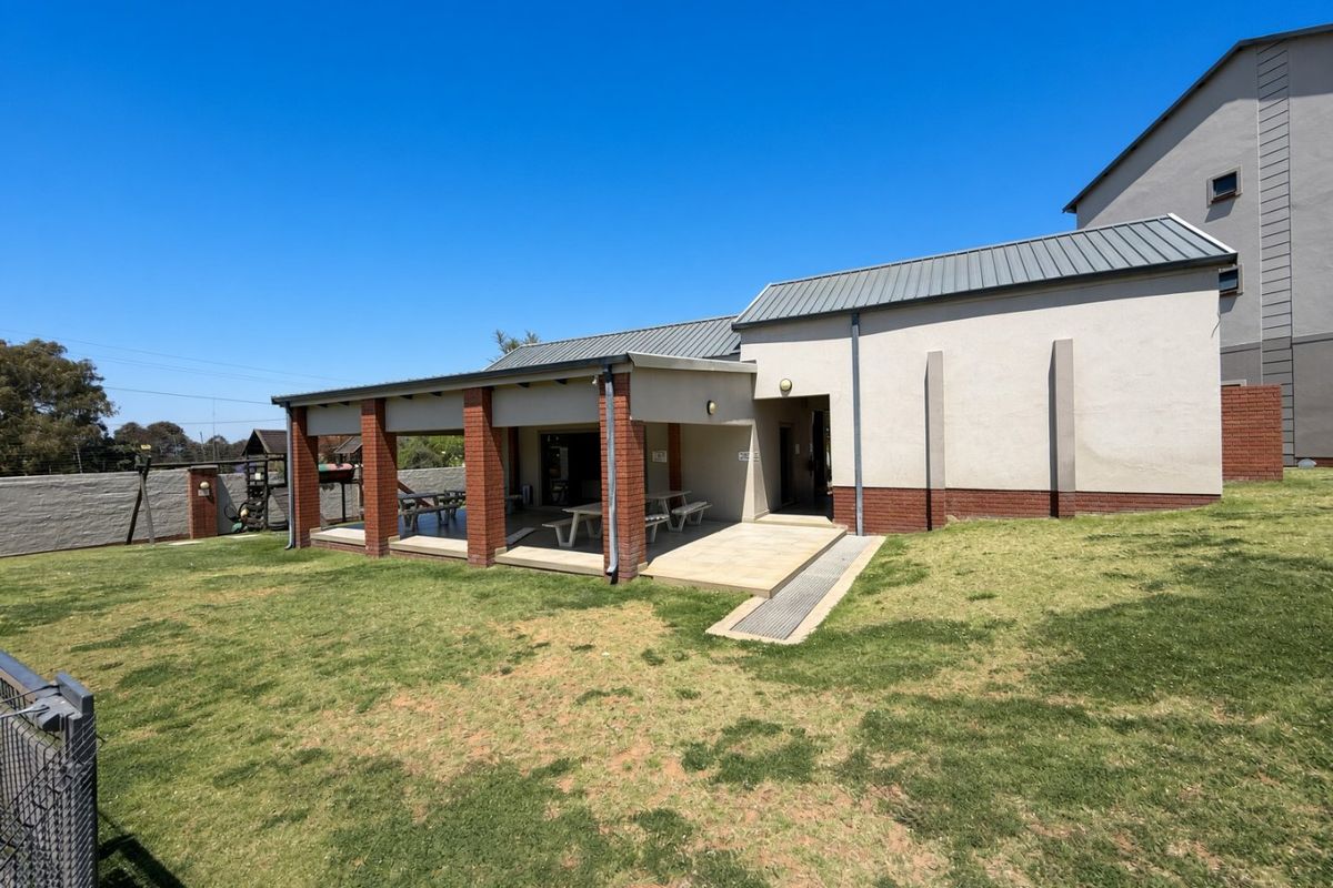 A rear view of the property featuring a covered patio area with brick pillars, a concrete slab, and a well-maintained lawn.