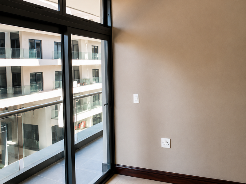 A bright, empty living area featuring large sliding glass doors that open onto a balcony, with neutral walls, tiled floors, and modern recessed ceiling details.