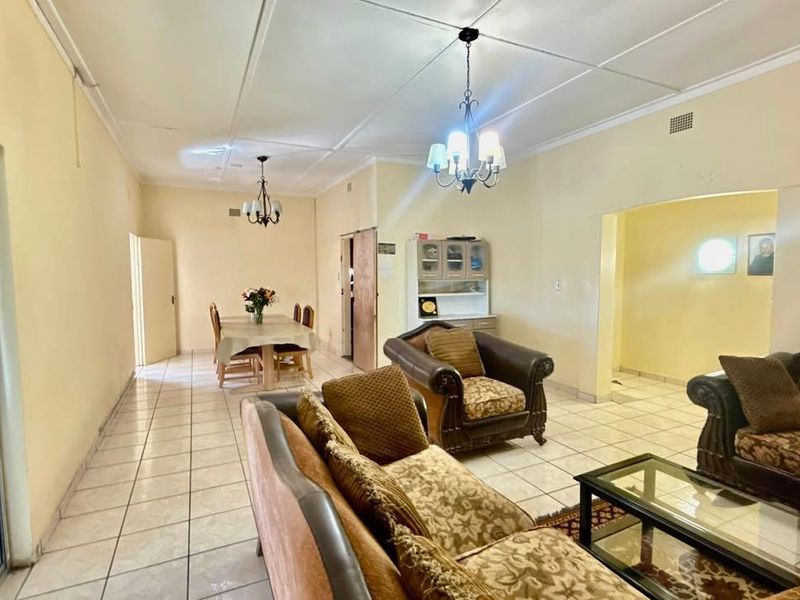 Spacious open-plan living and dining area featuring tiled flooring, ceiling cornices, and a built-in display cabinet, with access to the outdoors via a sliding door.
