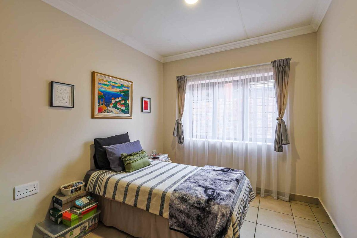 A well-lit bedroom featuring neutral wall tones, tiled flooring, and a large window with fitted curtains, providing a comfortable and functional living space.