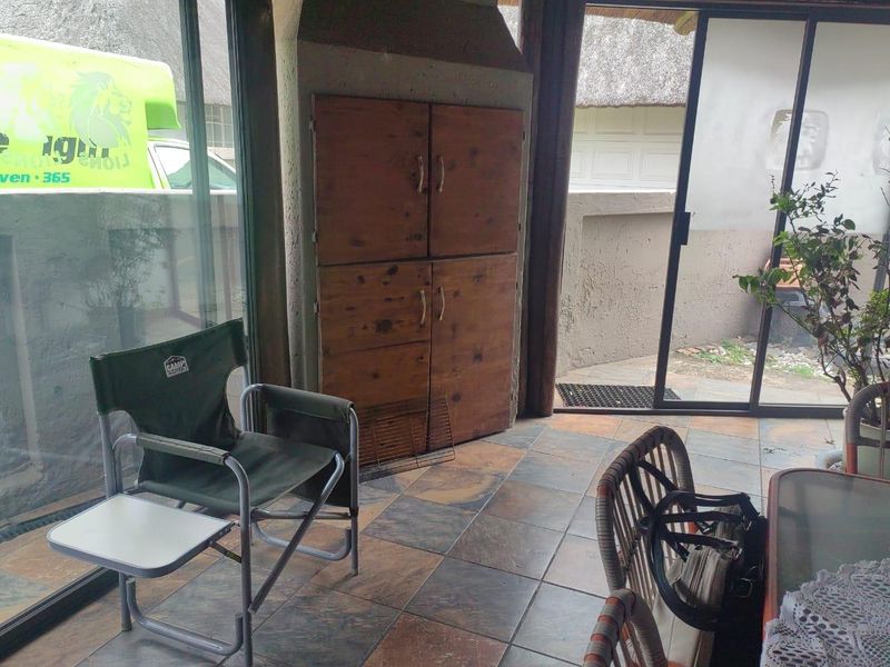 Covered patio area featuring a built-in braai, tiled flooring, and large sliding glass doors providing access to the exterior.