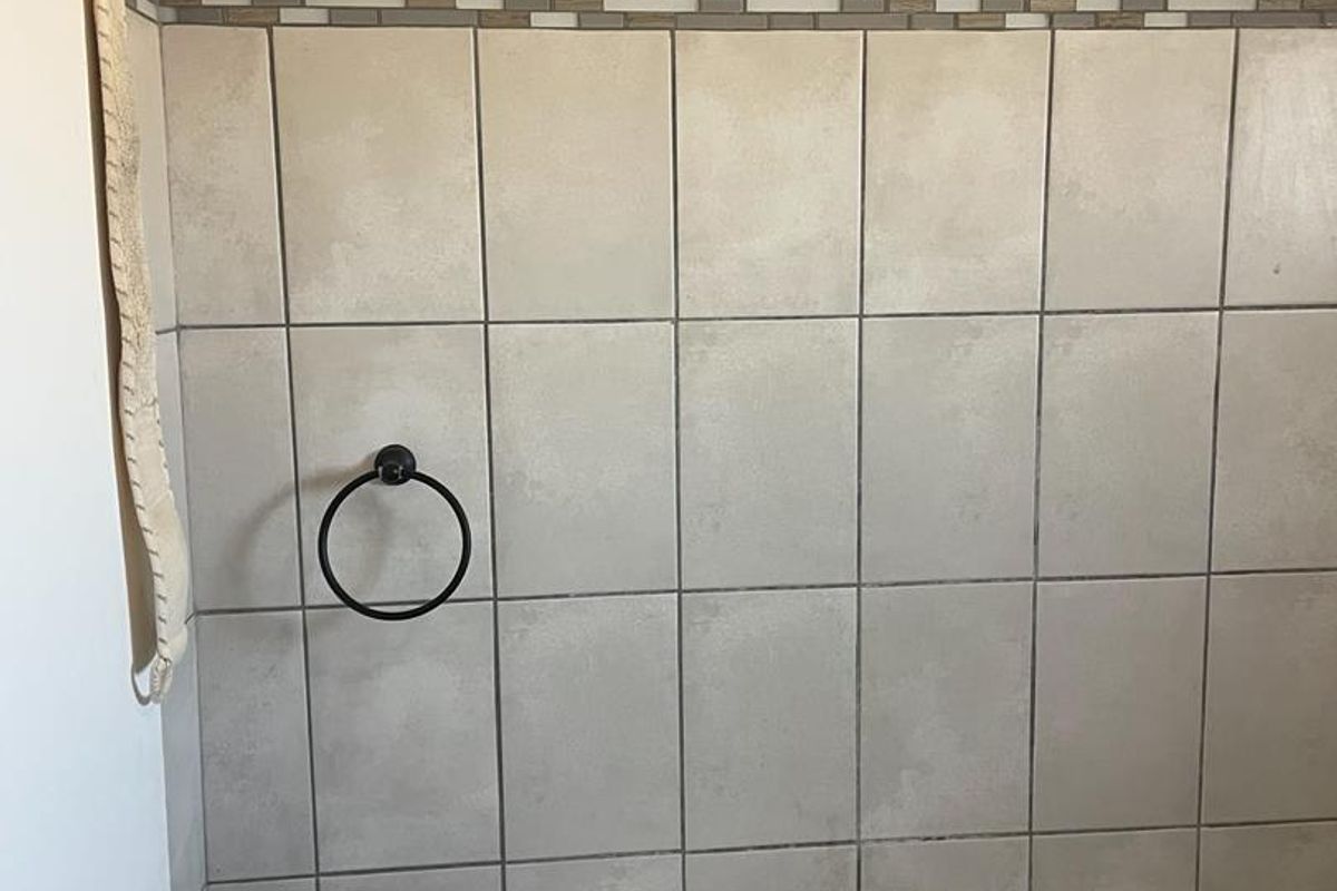 A bathroom featuring a wall-mounted basin with a mixer tap and neutral wall tiling with a decorative accent border.