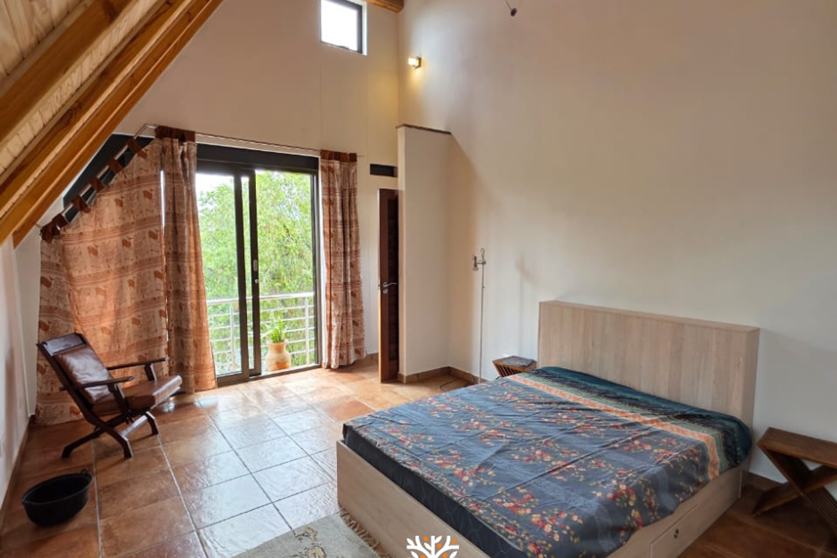Spacious bedroom featuring high vaulted timber ceilings, tiled flooring, and sliding glass doors leading to a private balcony with natural light.
