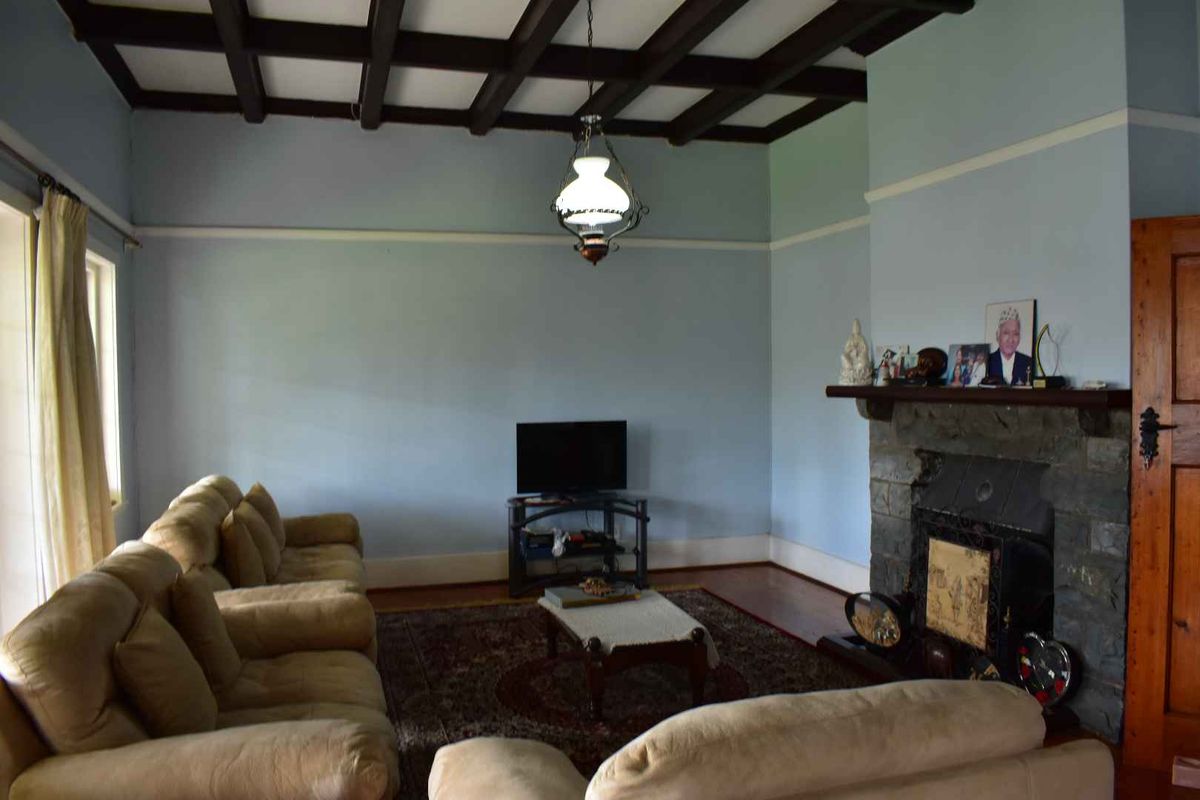 Spacious living room featuring a traditional stone fireplace, exposed timber ceiling beams, and polished wooden flooring.