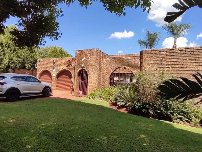 Front view of a face brick house featuring arched garage doors, a paved driveway, and a well-maintained front garden.