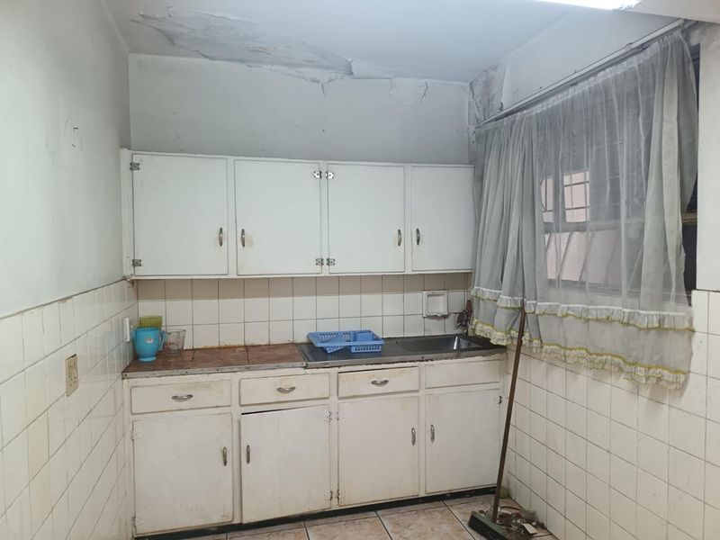A dated kitchen featuring original built-in cabinetry, tiled splashbacks, and a stainless steel sink, currently requiring significant renovation and ceiling repairs.