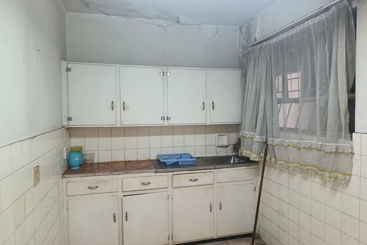 A dated kitchen featuring original built-in cabinetry, tiled splashbacks, and a stainless steel sink, currently requiring significant renovation and ceiling repairs.
