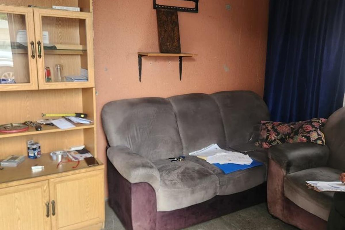 A living room area featuring tiled flooring and a ceiling fan, currently showing signs of wear on the wall surfaces.