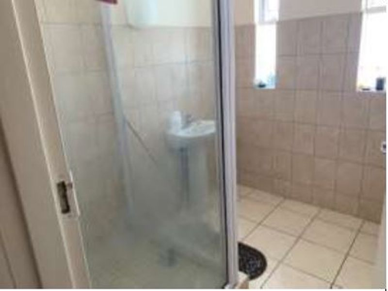 A functional bathroom featuring a pedestal basin, shower enclosure, and neutral wall and floor tiling.